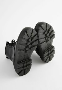 Bottines noires à semelles en caoutchouc texturé avec des crans profonds pour une meilleure adhérence, lacets ronds et surface supérieure en simili cuir lisse.