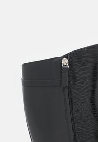 Schwarze Knöchelstiefel mit einer glatten Lederaußenseite und einem strukturierten, schlangenfellähnlichen Einsatz. Verfügt über einen seitlichen Reißverschluss und ein schmales Riemen-Detail.