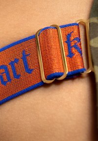 Orange strap with blue accents features woven text, secured with a gold metal buckle. The material has a coarse texture.