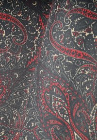 Tkanina z misternym wzorem paisley w kolorze czerwonym i beżowym na ciemnym tle; charakteryzuje się wyrazistymi spiralami i kontrastującymi kształtami w całej kompozycji.
