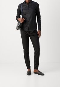 Maglietta nera a maniche lunghe, pantaloni neri slim-fit e mocassini neri. Tessuto morbido, taglio classico e dettagli in oro sulle scarpe.