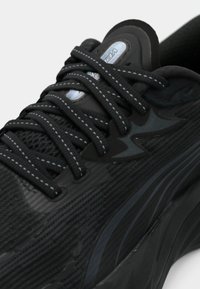 Mustast tekstuuriga kangast spordijalats lähivaates, paksu tallaga ja mustade pitsidega, millel on valged õmblused.