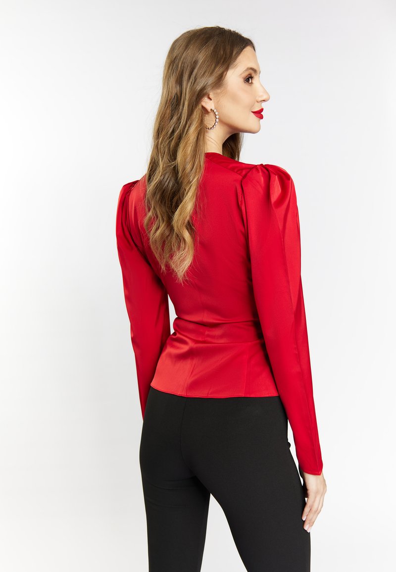 Rød satinbluse med strukturerede skuldre og lange ærmer, tætsiddende ved taljen, parret med sorte leggings, set fra ryggen.