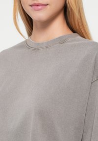 Γκρι βαμβακερό t-shirt με στρογγυλή λαιμόκοψη, κοντά μανίκια και άνετη εφαρμογή με εμφανείς ραφές. Ομαλή, μαλακή υφή.