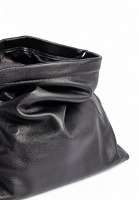 Juodas odinis krepšys su minkšta, sulenkta tekstūra. Dizainas pasižymi plačia angą ir lygia, nesurištą forma.