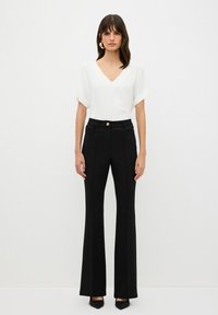 Witte v-hals blouse met korte opgerolde mouwen, gecombineerd met hooggerote zwarte flared broeken met voorzakken en een sluiting met gouden knopen.