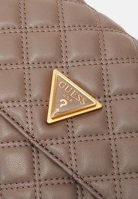 Matière en cuir marron matelassé avec coutures diagonales et plaque triangulaire du logo Guess USA bordée d'or.