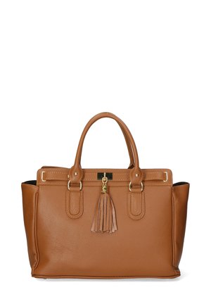 Braune Lederhandtasche mit strukturiertem Design, doppelten Tragegriffen und Quasten-Detail. Getragen über einem cremefarbenen Shirt und schwarzen Hosen, kombiniert mit weißen Sneakern.