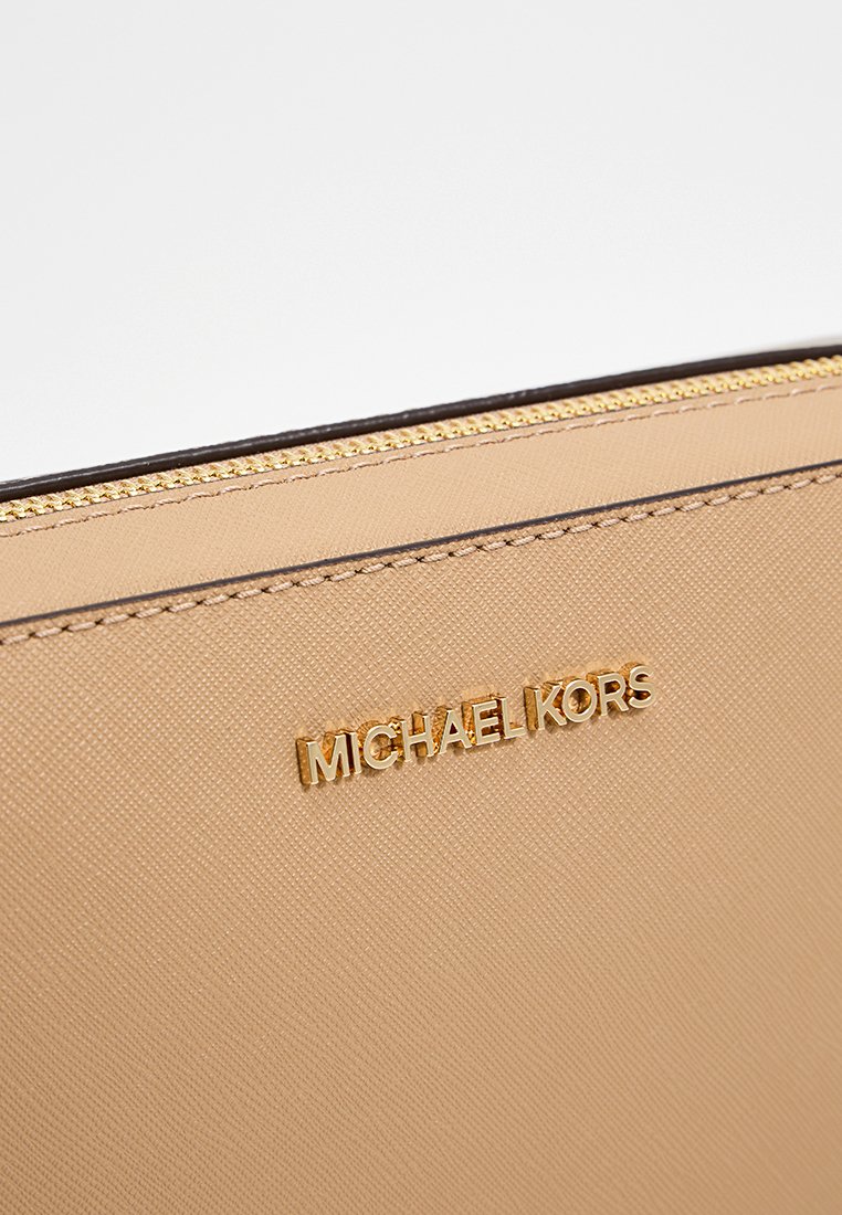 Portefeuille en cuir beige avec fermeture à glissière, présentant une surface texturée et une quincaillerie en ton doré avec le logo "MICHAEL KORS". Couture détaillée le long des bords.