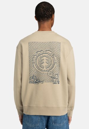 Beige sweatshirt med grafisk design av en tegelvägg med tecknade figurer och en pratbubbla, textilerad tyg och ribbade ärmslut.