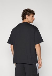 Svart t-shirt med korta ärmar och rund hals, med en avslappnad passform och mjukt tyg, sedd bakifrån utan synliga tryck.