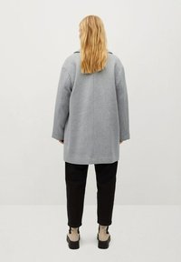 Szary wełniany płaszcz o luźnym kroju, szerokich rękawach i prostym fasonie. Dopełnieniem stroju są czarne spodnie i botki za kostkę.