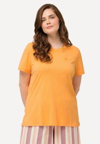 Camiseta de algodón naranja de manga corta y cuello redondo. Presenta un pequeño diseño bordado en el pecho. Textura suave.