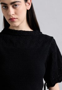 Top nero in maglia con motivi testurizzati, maniche corte a sbuffo e scollatura rotonda. Presenta dettagli sottili e una finitura in tessuto intrecciato.