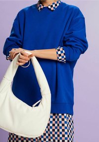 Sudadera azul con un cuello estampado, combinada con un bolso de hombro de cuero blanco con forma redondeada y cierre de cremallera.