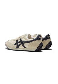 Scarpe sportive in suede beige con accenti blu navy, dotate di una suola testurizzata, collare imbottito e logo intrecciato. Design retro classico.