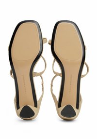 Sandalias de tacón alto en color beige con un acabado de ante suave, diseño abierto, correas estrechas y una suela de goma negra con una punta de tacón curvada.