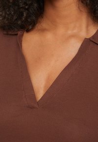 Brązowy top z żeberkowanego materiału z głębokim dekoltem w serek i krótkimi rękawami, z delikatnymi detalami przeszycia i gładką fakturą.