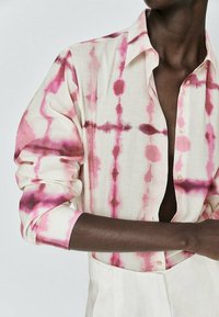 White linen shirt with pink tie-dye patterns, featuring a button-down collar and long sleeves, showcasing a lightweight, textured fabric.