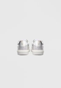 Αθλητικά παπούτσια με επάνω μέρος σε λαμπερό ασημένιο χρώμα με μεταλλική υφή, λευκές σόλες και διακριτικό λογότυπο στη φτέρνα.