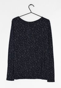 Marinblå långärmad topp med rund halsringning, prydd med ett spritt mönster av beige prickar, mjukt tyg och avslappnad passform. Hänger från en svart galge.