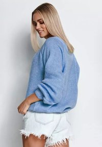 Jasnoniebieski sweter z dzianiny o luźnym kroju i oversize'owych rękawach, zestawiony z postrzępionymi szortami dżinsowymi, z fakturowanym wzorem.