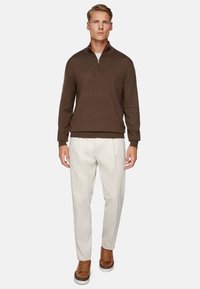 Dark brown knit sweater with a zippered collar, paired with light-colored, pleated trousers and brown lace-up shoes.