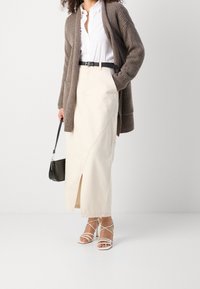 Beige kjol med framklipp, vit knäppt skjorta, brun ribbad cardigan, svart bälte och vita sandaletter med klackar. Svart väska.