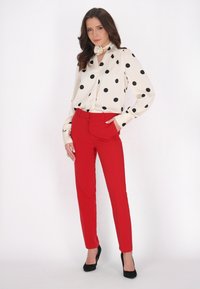 Blusa con pois neri su fondo crema, abbinata a pantaloni rossi su misura. Tacchi alti neri completano l'outfit.