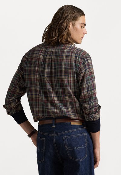 Ruitjesoverhemd met knopen in donkergroen, rood en beige; zachte stof; lange mouwen met marineblauwe manchetten; gestyled met blauwe jeans en een bruine riem.