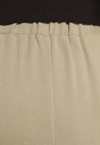 Tissu beige texturé avec une ceinture élastique froncée sous un bord de vêtement noir côtelé.