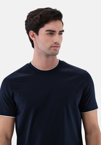 Marineblaues T-Shirt mit kurzen Ärmeln und rundem Ausschnitt, kontrastierend mit weißem Besatz, aus glattem Stoff gefertigt und mit figurbetontem Schnitt.