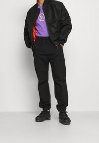 Black bomber jacket, purple t-shirt with yellow graphic, black cargo pants, and black sneakers. Features include elastic cuffs and pockets.