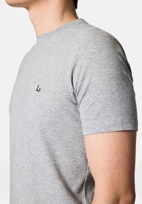 Szara koszulka z krótkim rękawem, wykonana z miękkiego materiału; posiada minimalistyczne czarne logo na górze po lewej stronie oraz klasyczny okrągły dekolt.