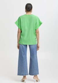 Top verde testurizzato a maniche corte abbinato a pantaloni in denim blu a gamba larga, caratterizzati da una vestibilità comoda e un orlo dritto.
