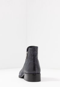 Stivale a caviglia in pelle di serpente nera con cerniera, superficie texturizzata e tacco basso impilato. Design semplice con finitura liscia e accenti minimi.