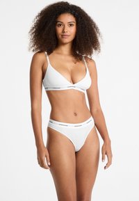 Weiße Bralette mit dünnen Trägern und dreieckiger Form, ausgestattet mit einem elastischen Band mit Logo; passender weißer Tanga mit Logo-Bund.