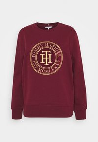 Bordeauxrode sweatshirt met een ronde goudkleurige geborduurde logo met tekst, geribbelde manchetten en een ronde halslijn. Zachte stof met een gladde textuur.