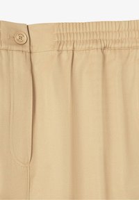 Beige byxor med en slät textur, elastisk midja och knappdetalj; har en sidoficka med en ren, skräddarsydd design.