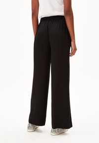 Pantalons larges noirs avec une taille élastique, présentant une texture lisse et portés avec des baskets affichant un motif zèbre.