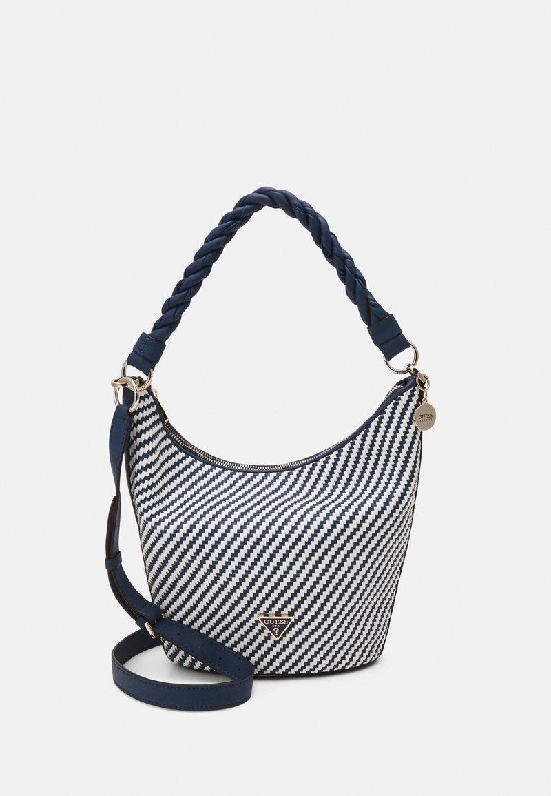 Navy and white herringbone-patterned shoulder bag with a braided handle, zip closure, and logo accent on front. Includes a detachable strap.