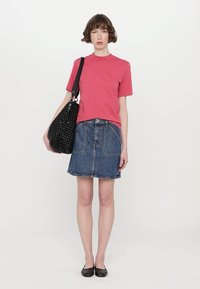 Red short-sleeve t-shirt paired with a blue denim skirt, featuring front pockets and a denim texture. Black woven tote bag. Black flats.