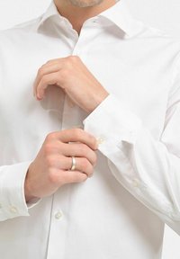 Vit skjorta med knappa ärmar och en mjuk struktur. Den har pärlknappar på ärmarna, klassisk krage och en figurnära design. Händer som justerar ärmarna.