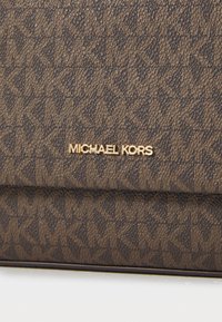 Brown textured material with a patterned design features the "MICHAEL KORS" logo in gold. Accents include glossy hardware and subtle raised details.