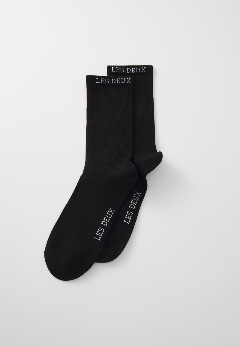 Sorte bomuldsstrømper med ribbet tekstur, der har hvid "LES DEUX" broderi øverst og på siden. Enkel design, mellemlang længde.