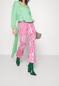 Zelený plisovaný zavinovací top v kombinaci s růžovými a bílými vzorovanými kalhotami s rozšířenými nohavicemi. Dokončeno lesklými zelenými botami na podpatku s krokodýlí texturou.