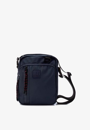 Bolso bandolera azul marino hecho de material resistente, con un frente texturizado, un parche de logo prominente y tiradores de cremallera en contraste rojo y negro.