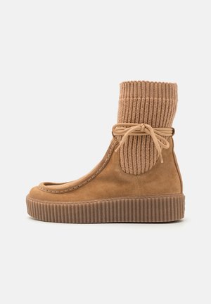 Botte en suède kaki avec bord côtelé en tricot et fermeture à lacets, présentant un bout rond et une semelle plateforme texturée. Convient pour un usage décontracté.