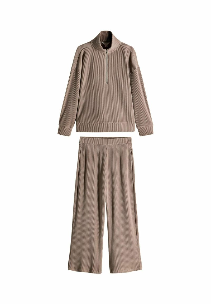 Completo loungewear beige a costine composto da una felpa con zip a un quarto e colletto alto e pantaloni a gamba larga, entrambi realizzati in tessuto morbido.