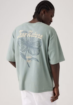 Camiseta oversize verde menta de algodón, con un gran motivo floral y el texto "True Nature" impreso en la parte trasera.